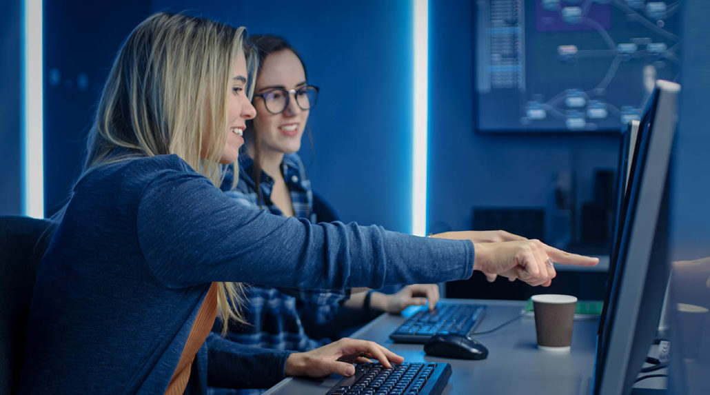 Two female cyber specialists discuss their cybersecurity careers at the office.